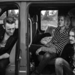 grayscale photo of three men sitting on vehicle seats