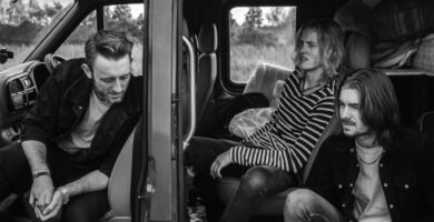 grayscale photo of three men sitting on vehicle seats